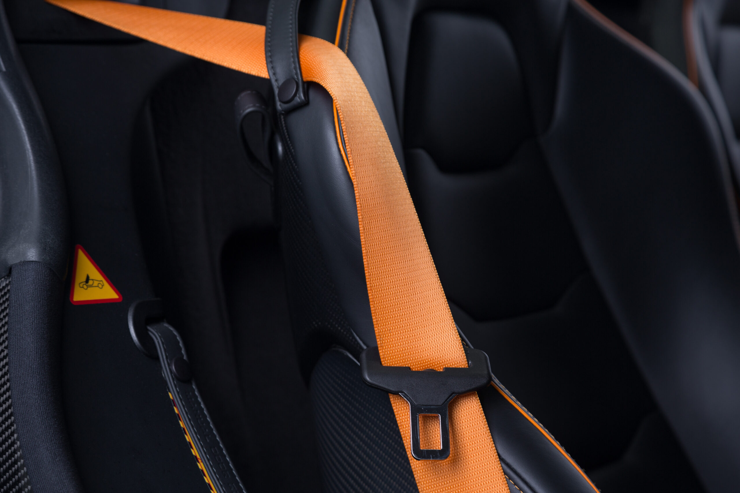 Close up of a black leather car seat with an orange belt